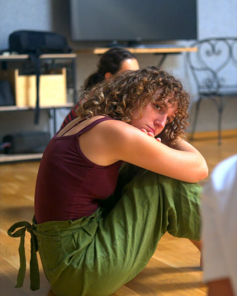 A student sitting on the floor hugs her knees during the lesson