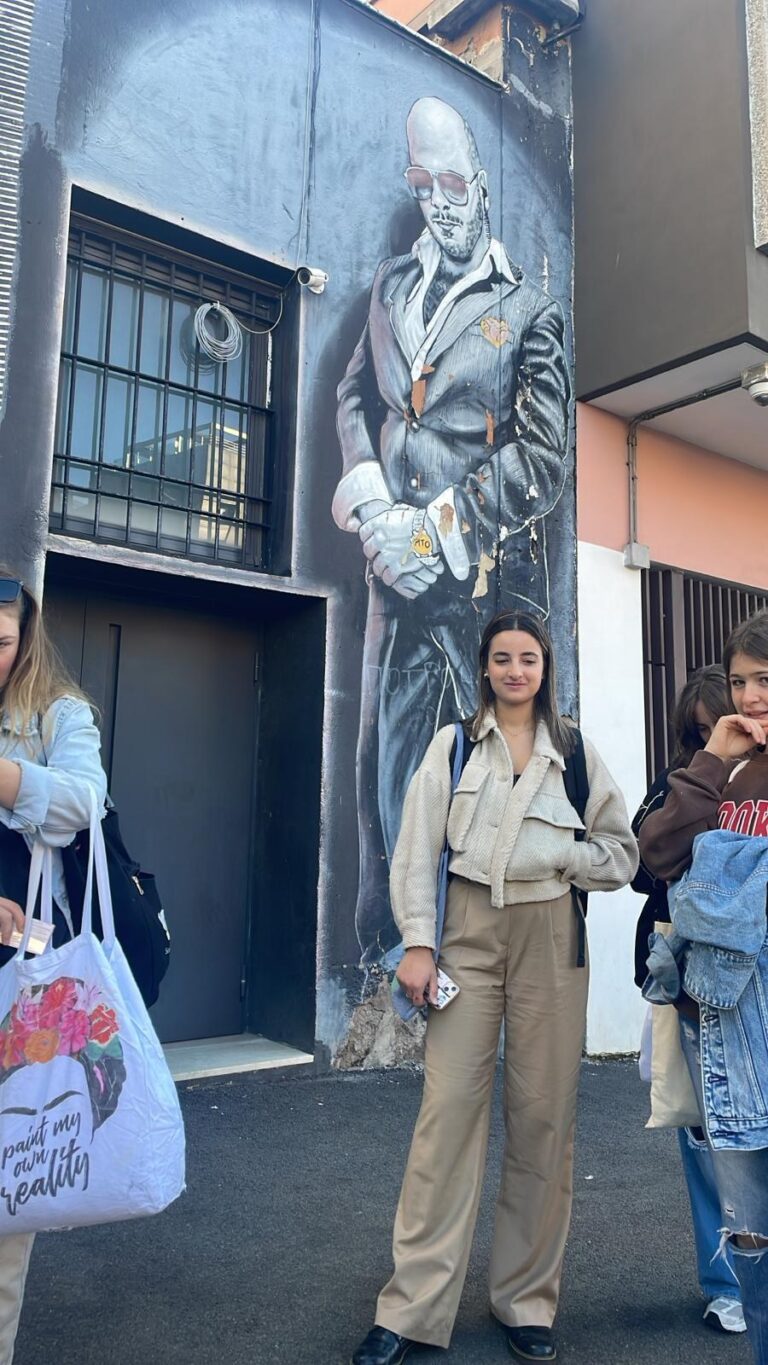 A student posing in front of the neighbourhood mural