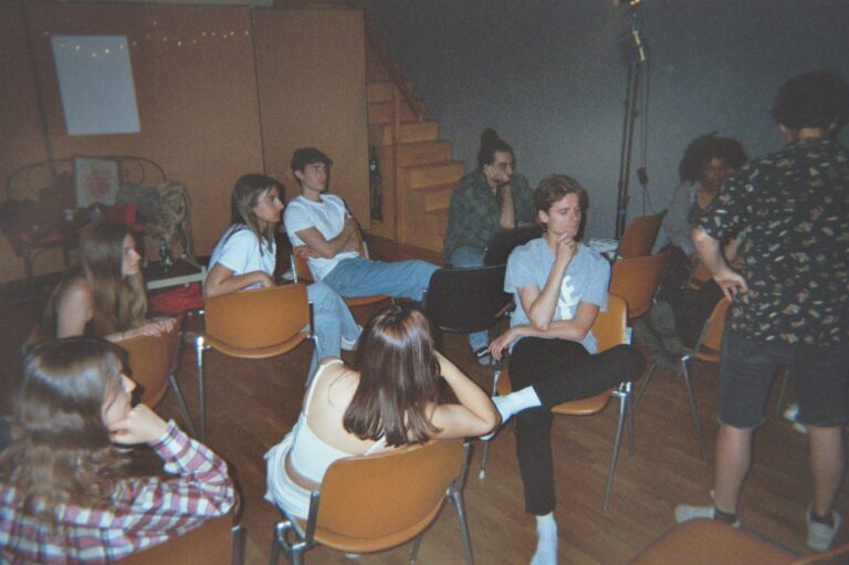 Students sitting in a circle on the orange chairs of the studio