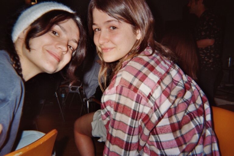 Two students smiling in the studio, one in a checked shirt