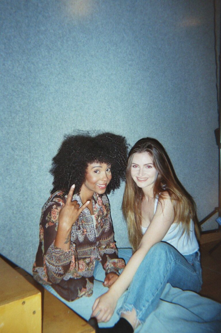 Two students sitting in front of the light-blue wall of the studio
