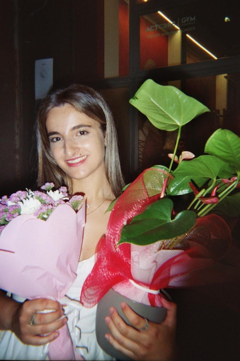 A student with a bunch of flowers and a plant in front of Actors Gym