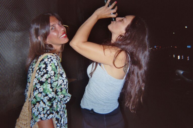 Two friends at night, one drinks from the bottle