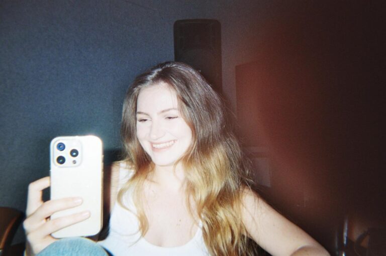 A student smiles while taking a selfie with her phone
