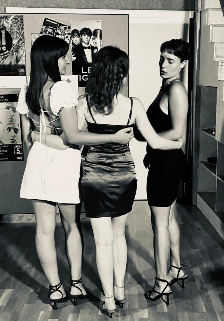 In black and white, three students hugging, seen from behind