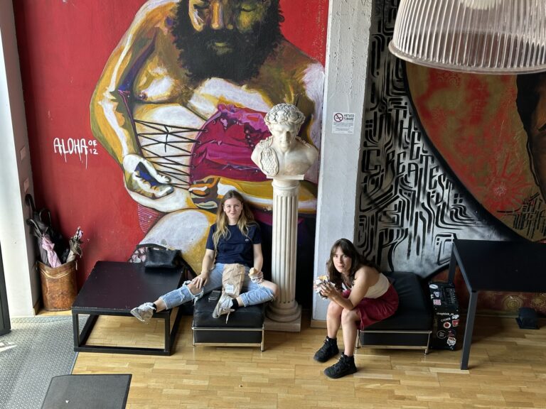 Two students in the entrance in front of the red Mob Studios mural