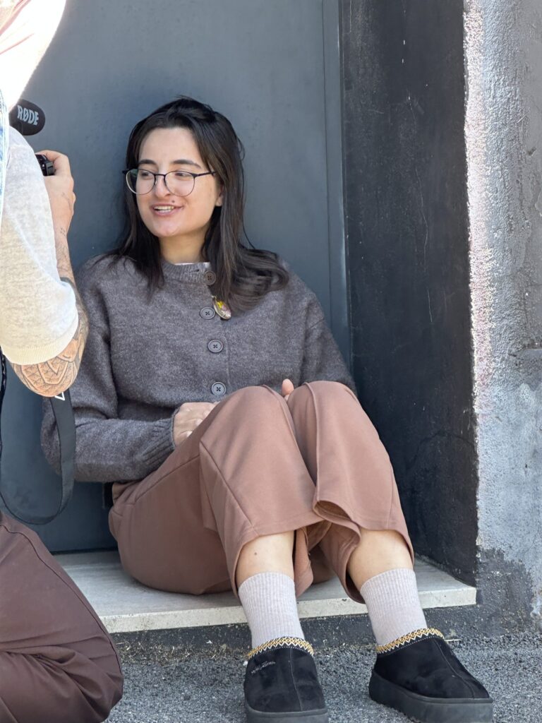 A student with glasses sitting in the sun on the street during the shooting of Luogo di Mezzo