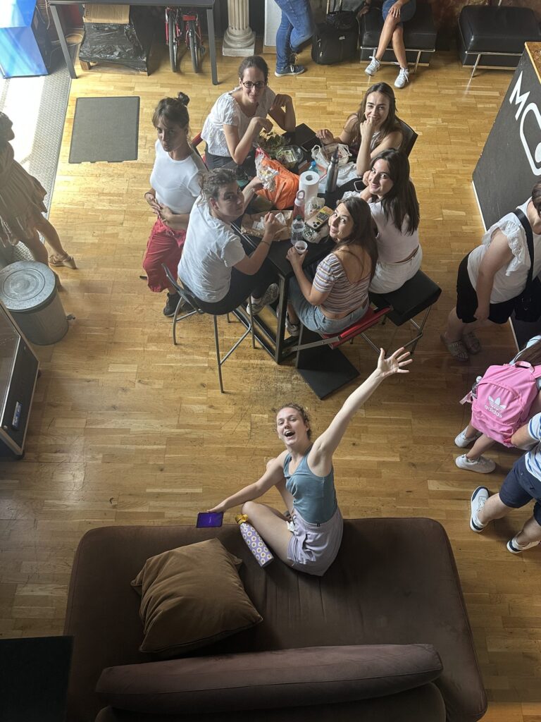 Lunch break at Mob Studios: a student on the sofa raises her arm, the group at the table looks at the camera
