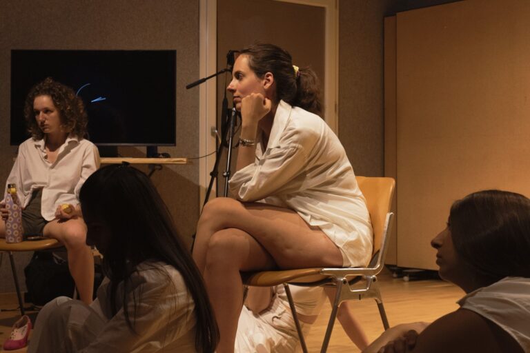 Persona: Performer seduta in sala con mano sul mento