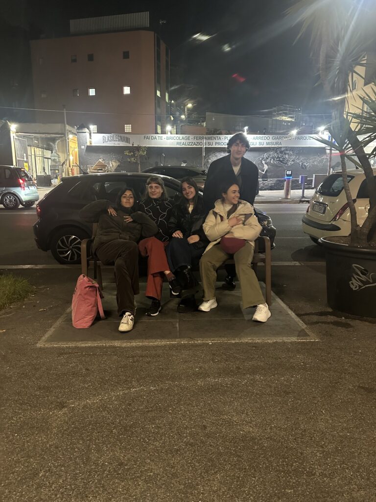 Four students sitting on the bench outside Mob Studios, in the evening