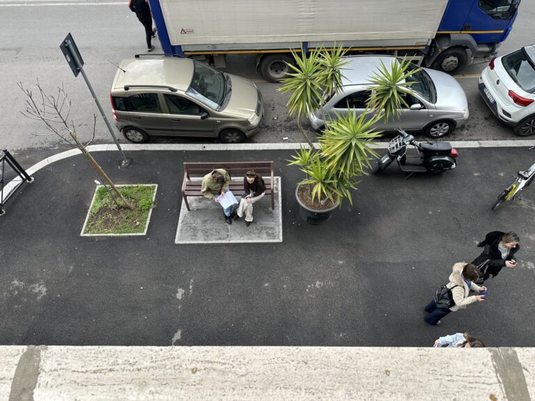 Two people on the bench outside Mob Studios, seen from the window