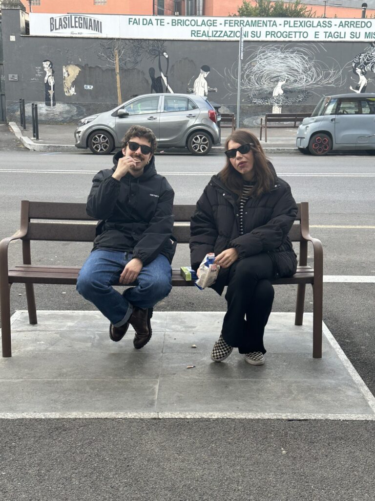 Two students in sunglasses sitting on the bench outside Mob Studios
