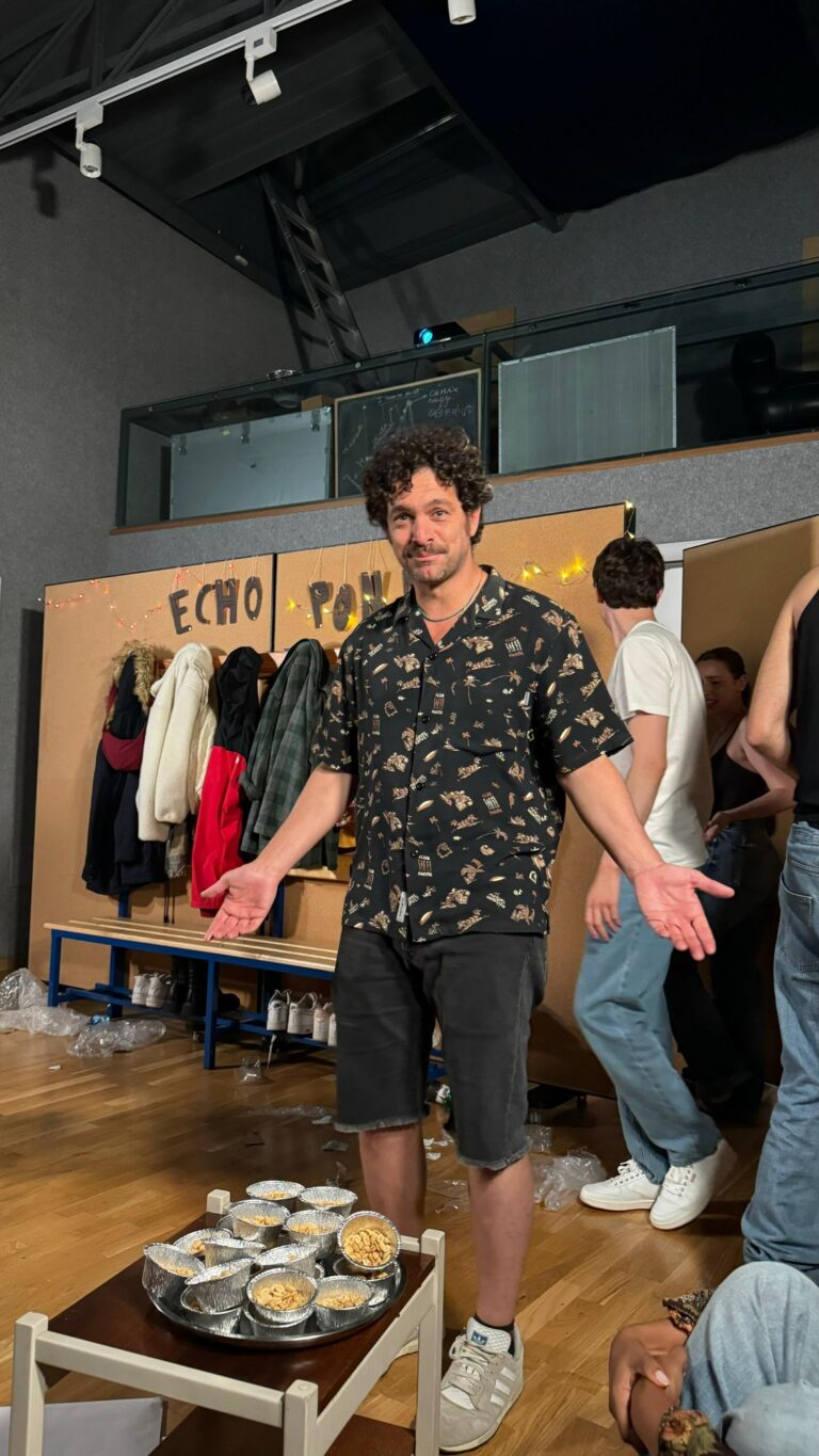 The trainer with open arms in front of the Almost Maine set, with a tub of peanuts